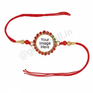 A blank personalized Rakhi from Glow Mall with a red and green jewelled frame, golden beads, and a white center ready for photo customization.